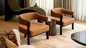 Deux fauteuils à motifs avec des pieds en bois, une table ronde en bois et une chaise verte moderne dans une pièce bien éclairée, agrémentée de rideaux.
