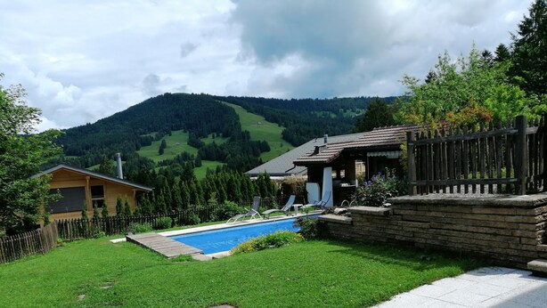 A backyard with a swimming pool, a wooden deck, and a stone wall. - Le Logis du bChalet Perce-Neige Route de la Cierne 91Les Paccots 1619 (Châtel-Saint-Denis)