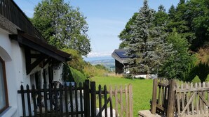 A rustic wooden gate leading to a paved pathway, surrounded by lush greenery and a white building with a dark roof. - Le Logis du bChalet Perce-Neige Route de la Cierne 91Les Paccots 1619 (Châtel-Saint-Denis)