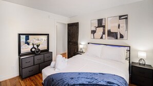 Ein Schlafzimmer mit Bett, Schminktisch, Fernseher und abstrakten Wandbildern.