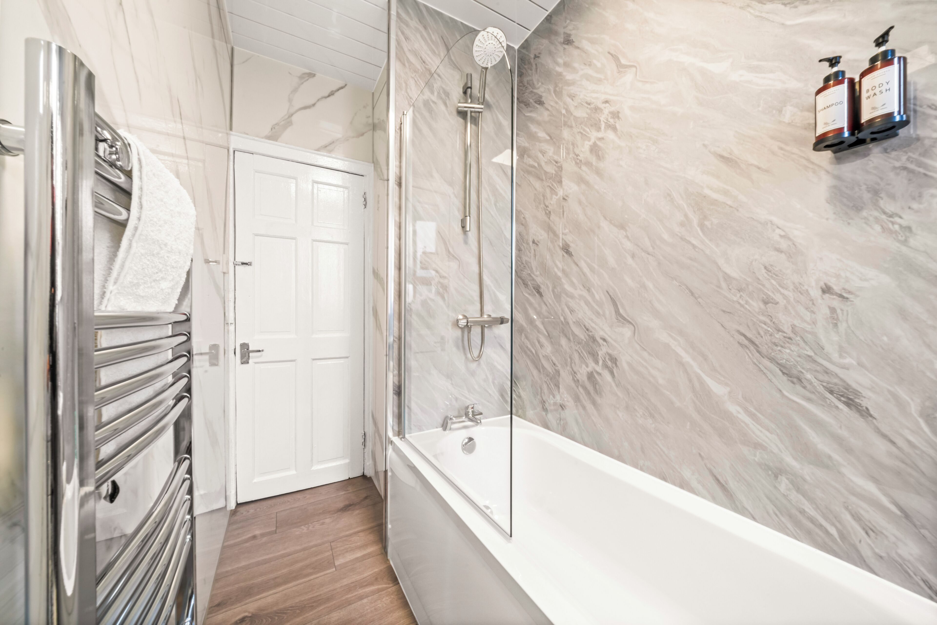 A modern bathroom with a glass-enclosed shower, a white bathtub, and a marble wall.