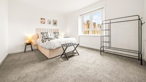 Ein Schlafzimmer mit einem Bett, einem Nachttisch mit Lampe, einem Fenster und einem Wäscheständer.