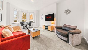 Ein modernes Wohnzimmer mit einem roten Sofa, einem braunen Ledersessel, einem Holztisch und einem an der Wand befestigten Fernseher.