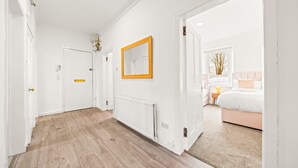 Ein Korridor mit Holzboden, weißen Wänden und einer Tür zu einem Schlafzimmer mit Bett und Nachttisch.