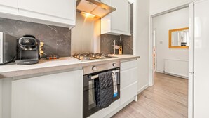 Eine moderne Küche mit weißen Schränken, einem Gasherd, einem Backofen und einer Kaffeemaschine.