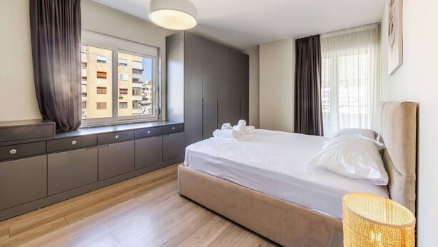 Una habitación de hotel moderna con una cama grande, una ventana con cortinas, un armario y una lámpara colgante.