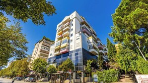 Un edificio de varios pisos con balcones, una parada de autobús y un letrero de clínica dental.