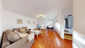 A modern living room with a sofa, coffee table, and TV. There is a dining area with a table and chairs. The room has wooden flooring and white walls. - Edenhome + 1 parking lot (Colmar)