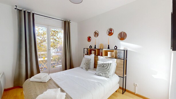 A bedroom with a bed, curtains, a window with a view, and wall decor. - Edenhome + 1 parking lot (Colmar)