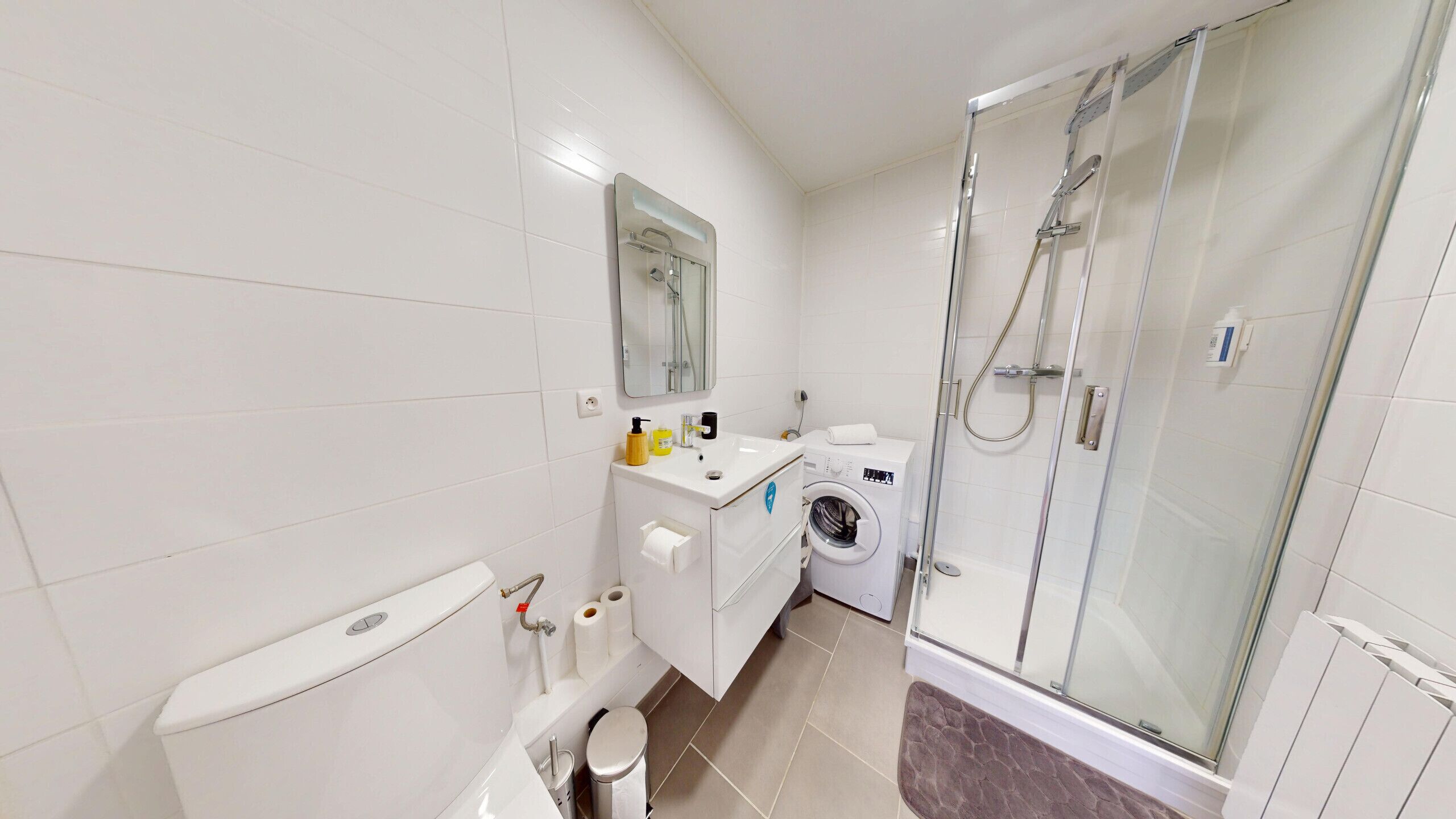 A modern bathroom with a toilet, sink, washing machine, and glass-enclosed shower.