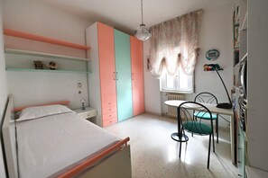 Un dormitorio con una cama, un escritorio con silla, un radiador y una ventana con cortinas.