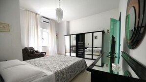 A bedroom with a bed, a chair, a dresser, a mirror, and a sliding door leading to a balcony. - GuestHost - Roomy and bright 140 sqm apartment, accommodating up to 4 people, located on the first floor of a building without an elevator.The property is located in a semi-central area of ​​Matera, well-served by public transport and a short distanc (Matera)