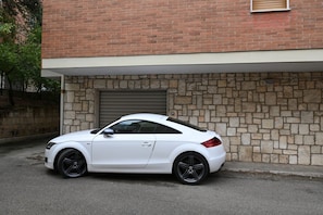 Un coche blanco estacionado frente a un edificio de fachada de piedra y puerta de garaje.