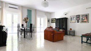 A spacious living room with a sofa, a dining table with chairs, a chandelier, and artwork on the walls. - GuestHost - Roomy and bright 140 sqm apartment, accommodating up to 4 people, located on the first floor of a building without an elevator.The property is located in a semi-central area of ​​Matera, well-served by public transport and a short distanc (Matera)