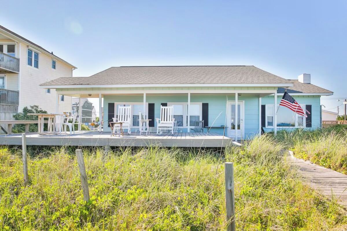 A coastal house with a covered porch, an American flag, and a wooden deck.