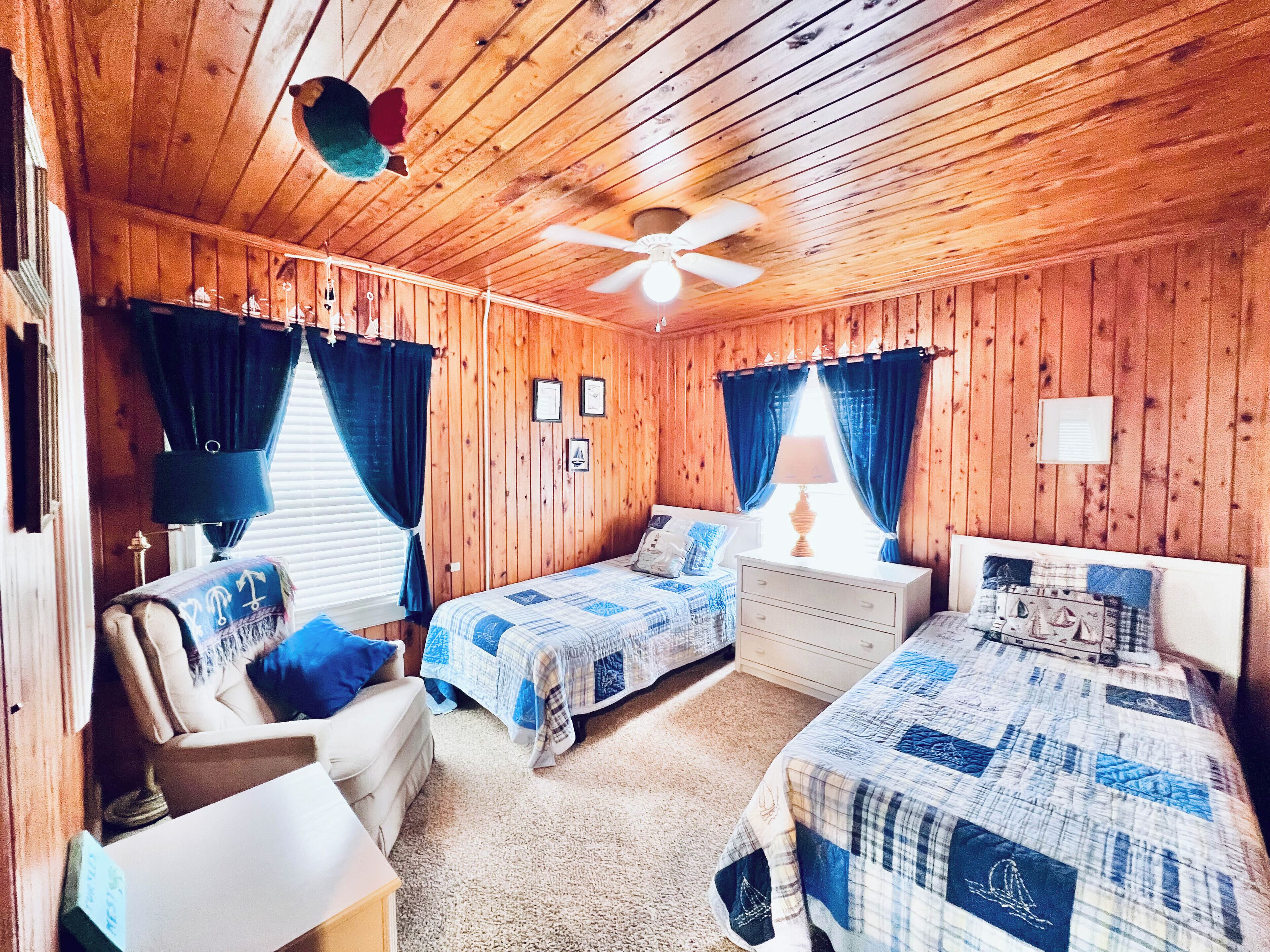 A cabin-style bedroom with two beds, a ceiling fan, and wooden walls.