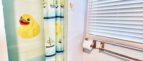 A bathroom with a shower curtain featuring a duck design, a toilet, and a window with blinds.