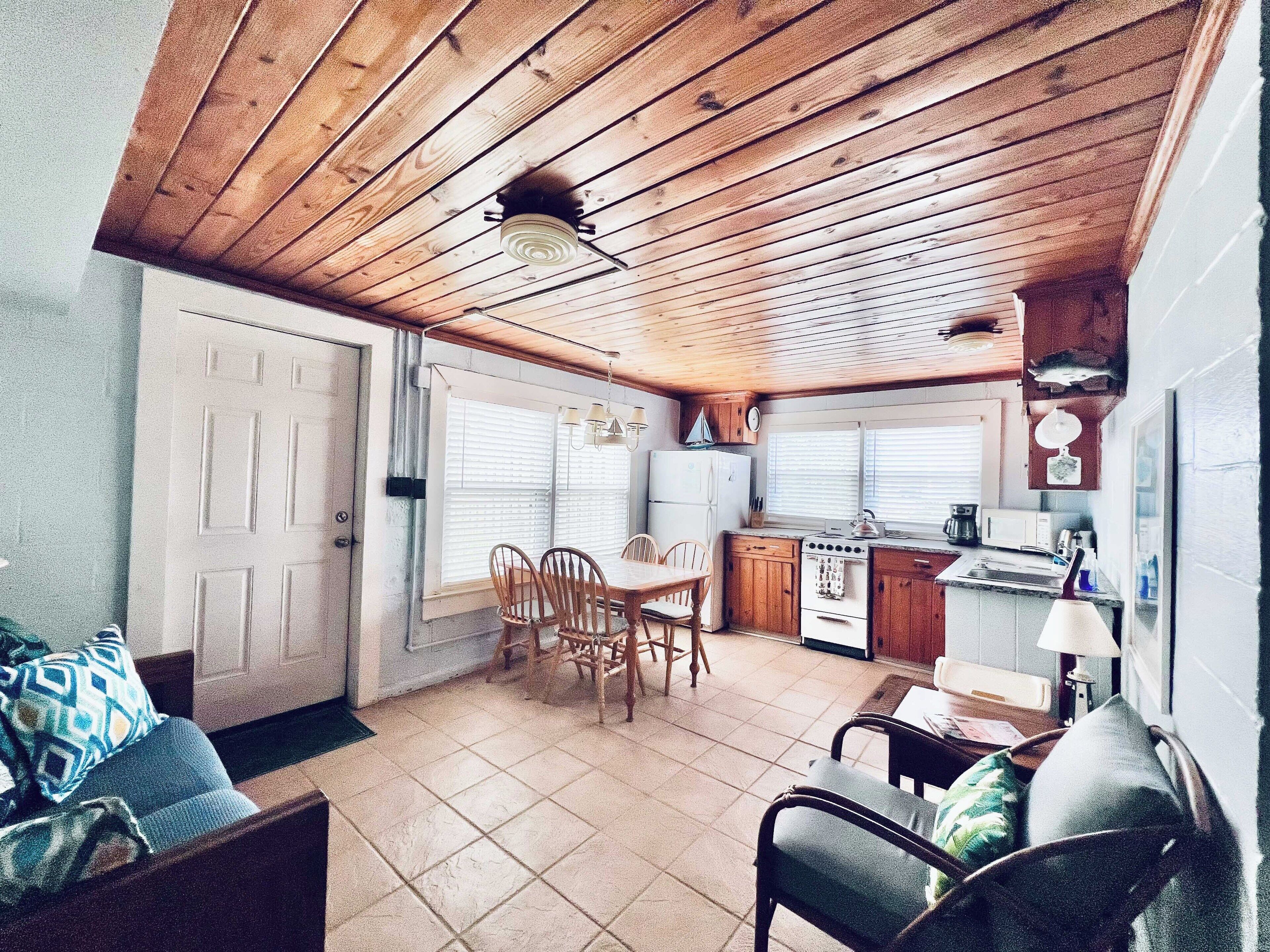 A compact kitchen with wooden cabinets, a stove, and a sink. There is a dining area with a table and chairs.
