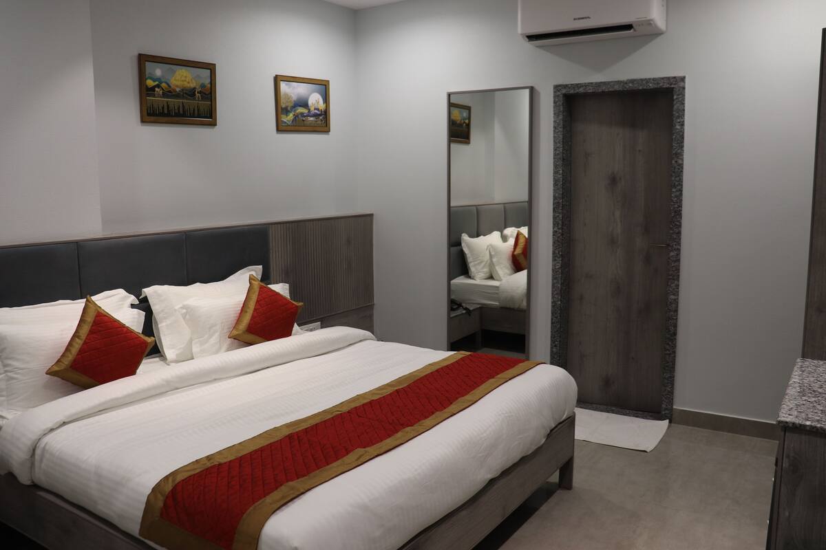 Habitació d'hotel amb un llit gran, una tauleta de nit, un mirall i una porta.