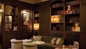 Una biblioteca acogedora con un sofá verde, sillas de mimbre y estanterías llenas de libros.