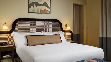 A neatly made bed with a checkered headboard, two bedside lamps, a framed artwork above the bed, and a magazine on the bed.
