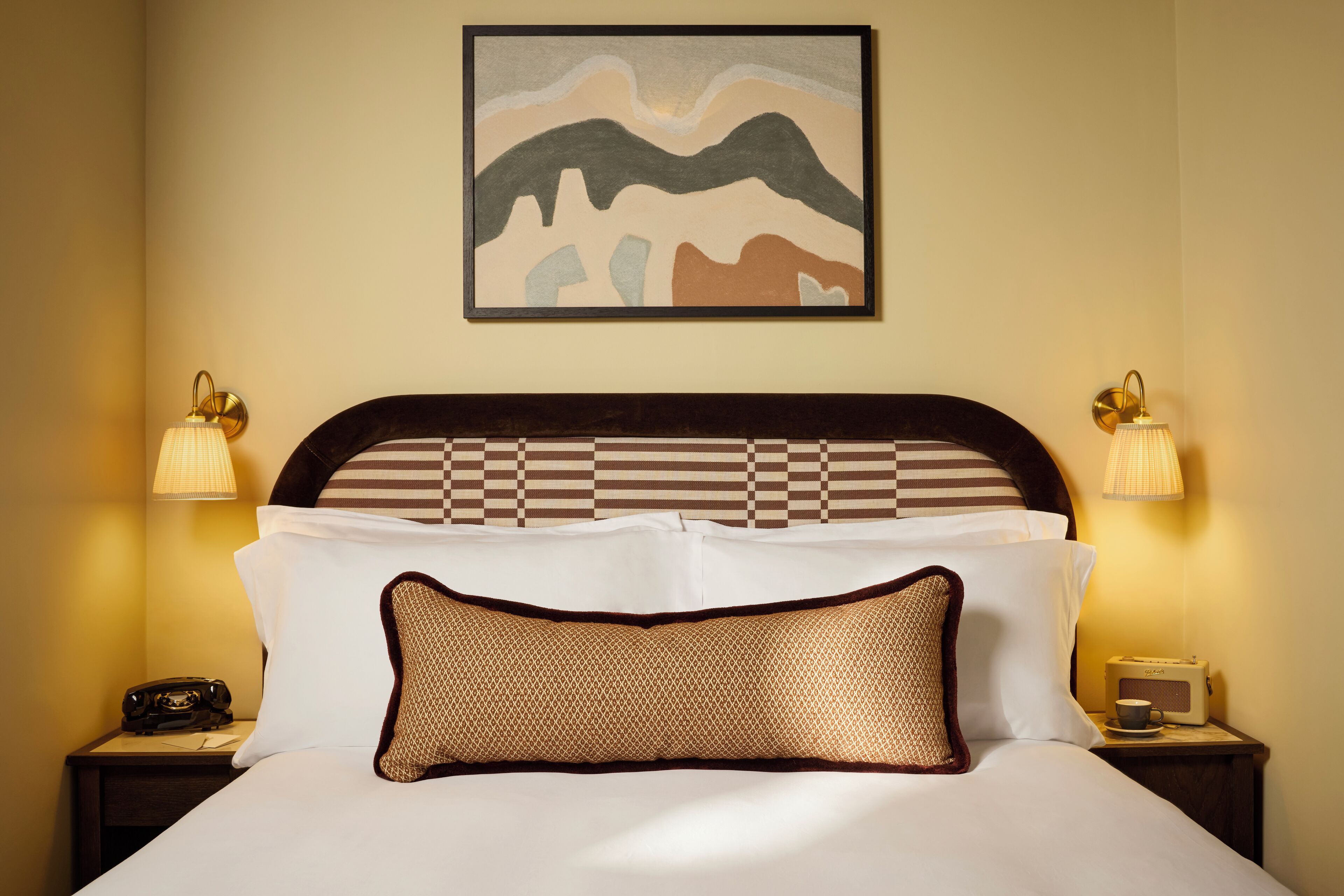 A neatly made bed with a checkered headboard, two bedside lamps, and a framed artwork above.