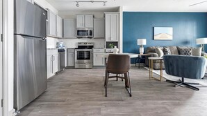 A modern kitchen with stainless steel appliances, a dining area with a blue sofa and a small table, and a blue accent wall. - Landing | Spectacular 1BD, Clubhouse, Game Room (Charlotte)