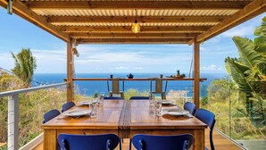 A wooden table set for dining with chairs, overlooking a scenic ocean view.