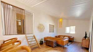 A modern living room with a wooden staircase, a sofa set, a coffee table, and a hanging light fixture.