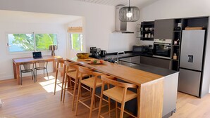 A modern kitchen with a wooden island, bar stools, a laptop, and a large window with a view of greenery.
