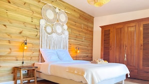 A bedroom with a wooden headboard, a bed with white linens, two bedside lamps, a wooden nightstand, and a large wardrobe.