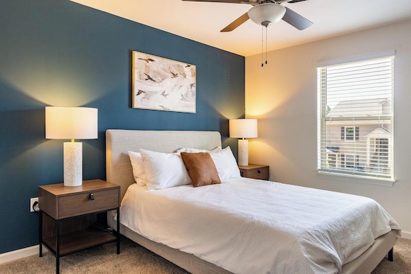 A bedroom with a bed, two bedside tables, a ceiling fan, and a window with blinds.