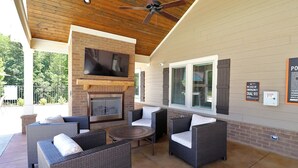 Un patio al aire libre con mobiliario de mimbre, una chimenea y un ventilador de techo.