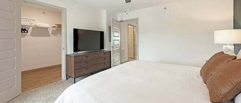 A bedroom with a bed, a TV on a dresser, a ceiling fan, and a closet with a laundry basket.