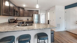 Una cocina moderna con armarios de madera oscura, electrodomésticos de acero inoxidable, encimera de granito y una zona con taburetes de bar.
