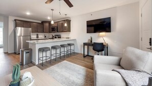 A modern kitchen with a central island, bar stools, and a dining area with a sofa and a TV.