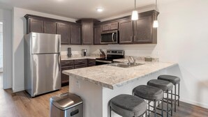 A modern kitchen with dark wood cabinets, stainless steel appliances, a granite countertop, and a bar stool area.
