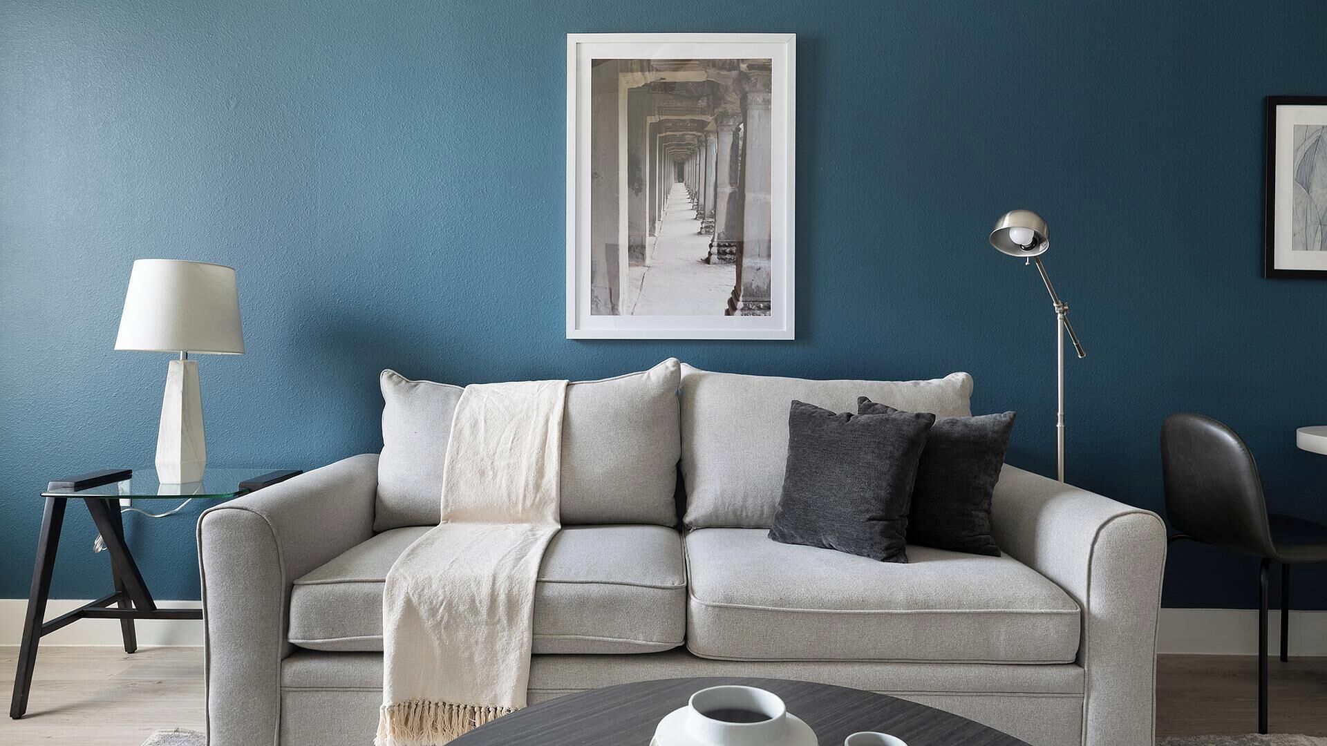 A modern living room with a grey sofa, a white throw blanket, and a coffee table with a white mug.