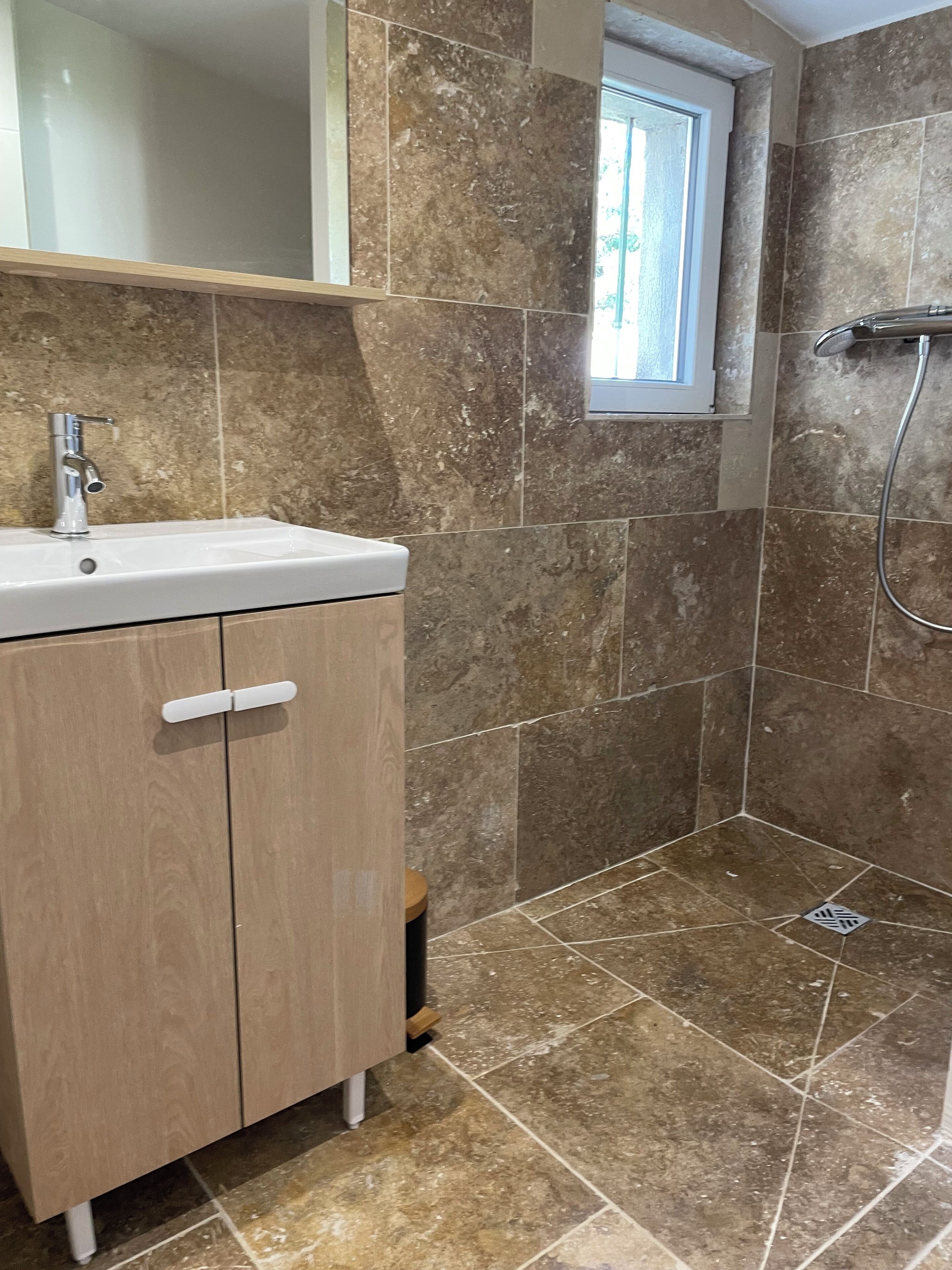 A bathroom with a sink, mirror, shower, and tiled walls.