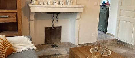 A living room with a sofa, coffee table, fireplace, and a shelf with decorative items.