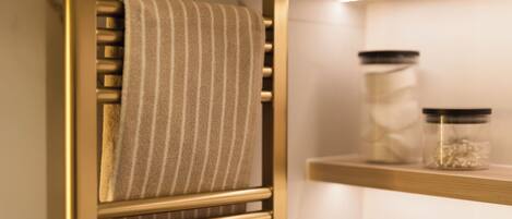 A bathroom with a towel rack, a shelf with jars, and a wooden shelf.