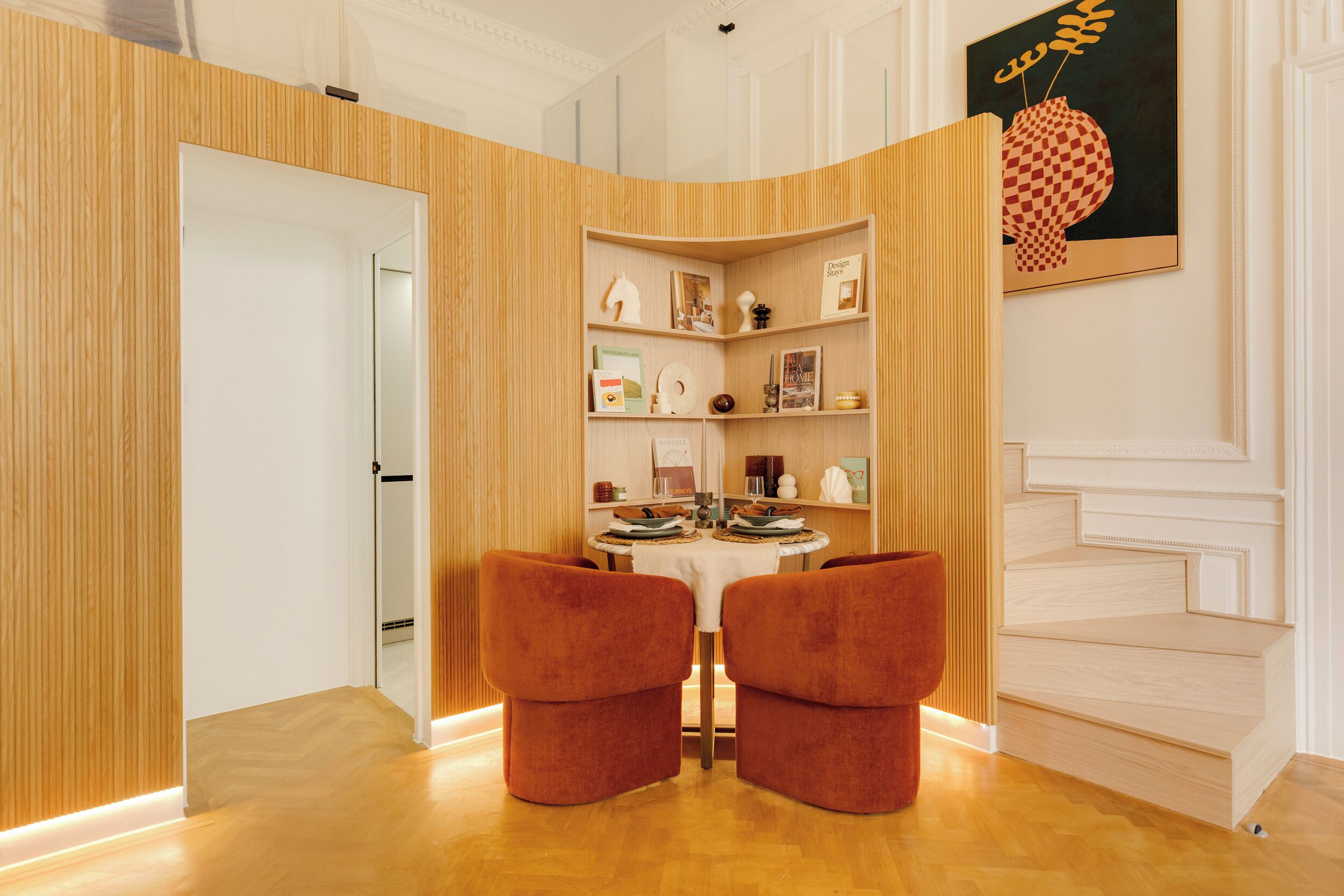 A modern dining area with a wooden accent wall, a round table, and two red chairs.