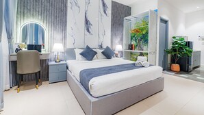 A modern bedroom with a large bed, a desk with a chair, a vanity with a mirror, and a potted plant.