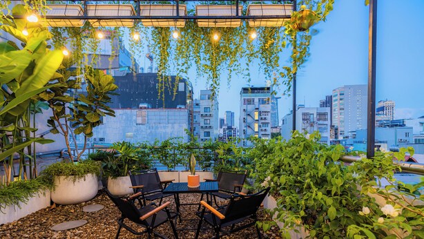 An outdoor seating area with a table and chairs, surrounded by potted plants and a cityscape view.