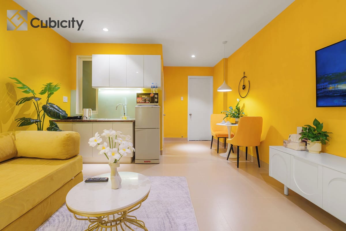 A modern living room with a yellow sofa, a white coffee table with flowers, and a dining area with yellow chairs.