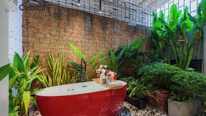 A red bathtub in a spa area with a brick wall and various plants around.
