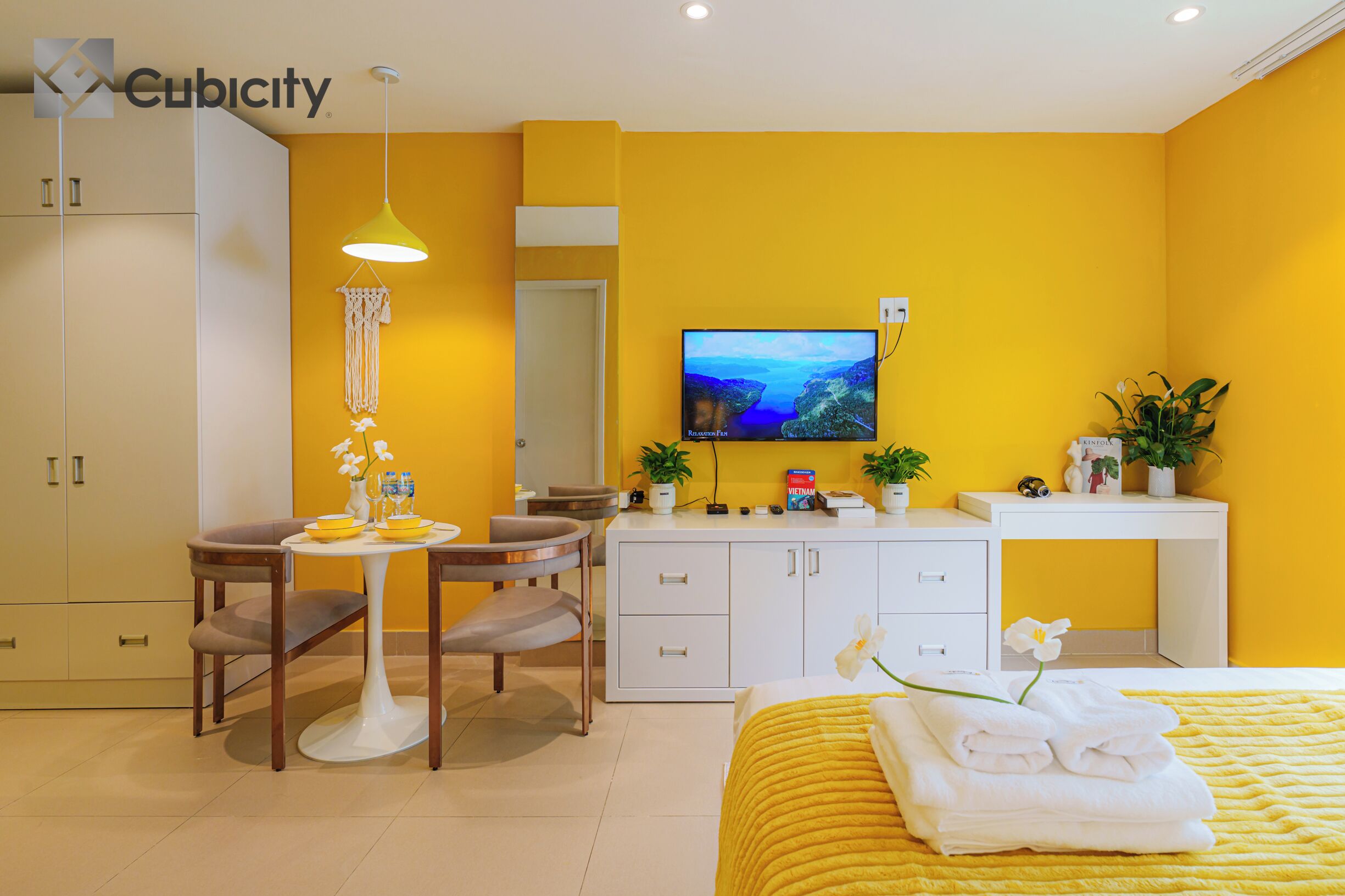 Habitación de hotel con decoración amarilla, que incluye una cama con cubrecama amarillo, un escritorio con silla, un televisor y un armario.