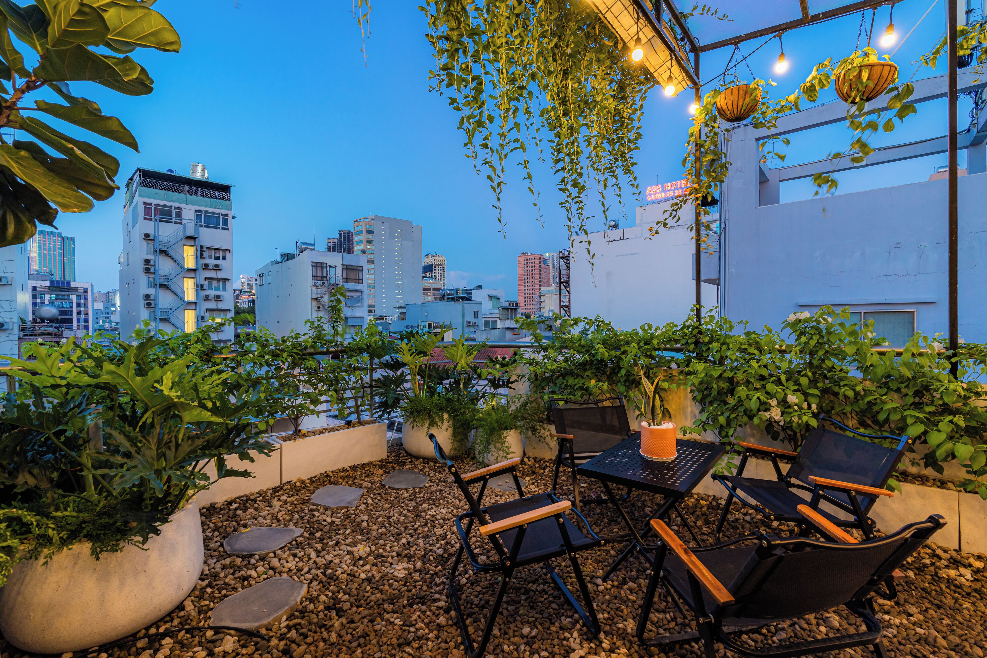 Un área de estar al aire libre con mesas y sillas, rodeada de plantas en macetas y vistas a la ciudad.