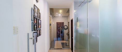 A hallway with glass walls, a clock, and framed pictures on the left wall.