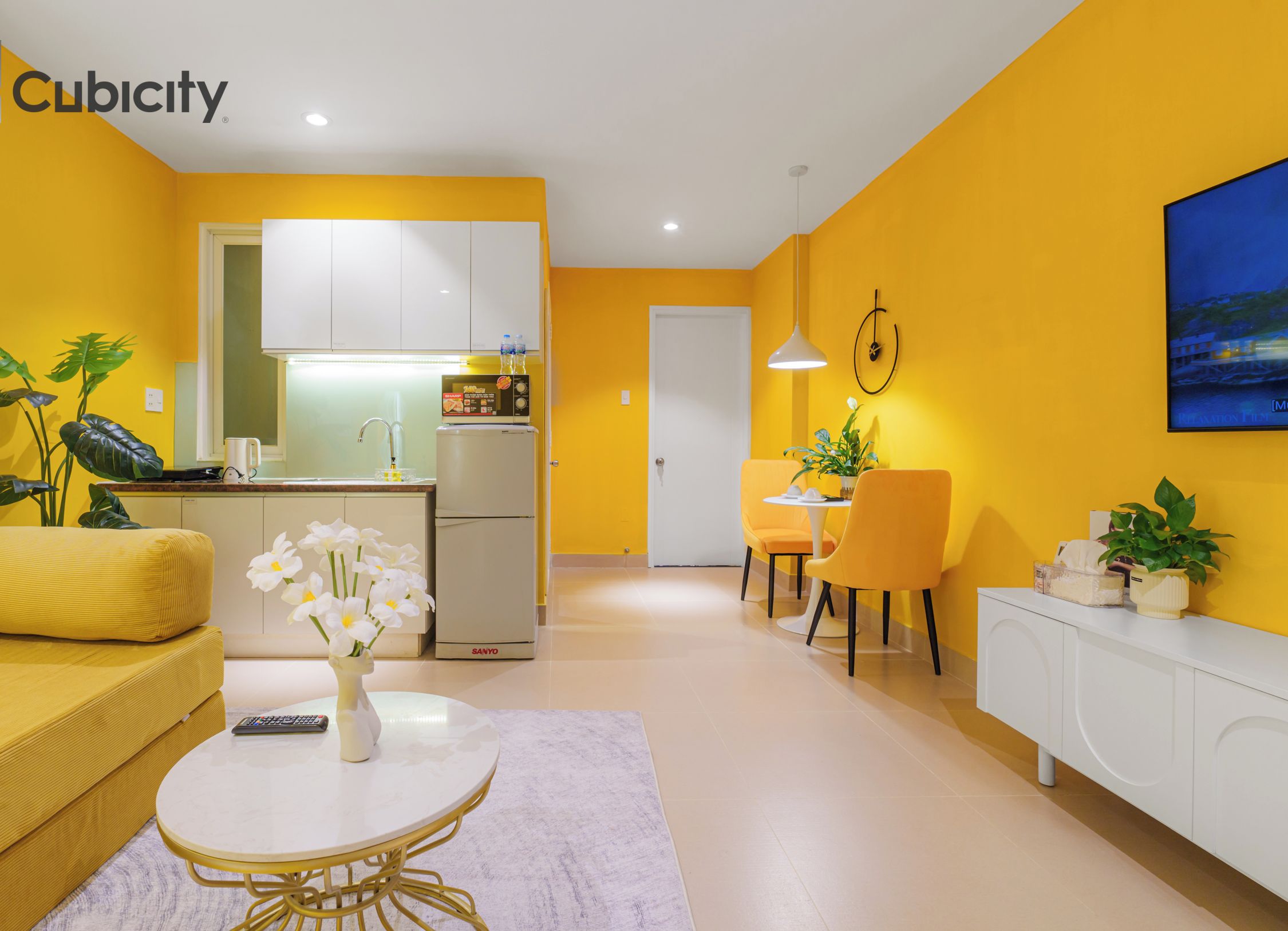 A modern living room with a yellow sofa, a white coffee table with flowers, and a dining area with yellow chairs.